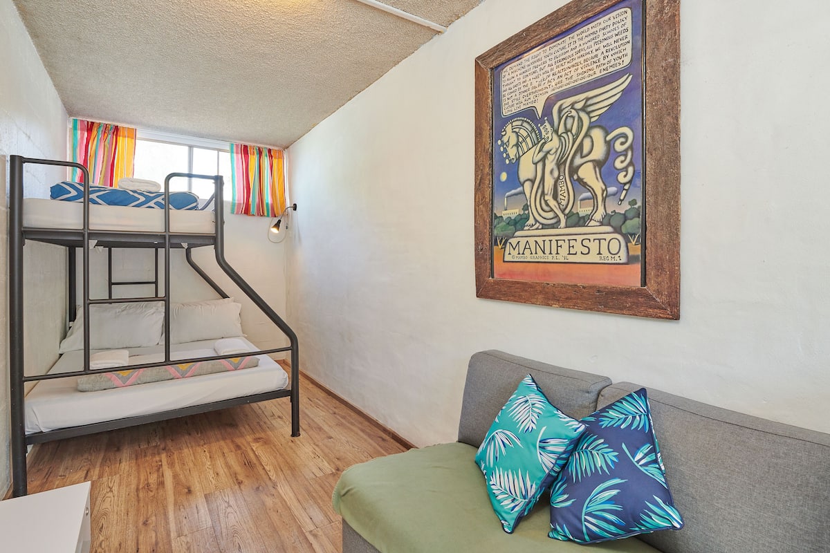 A bunk bed, a sofa with patterned cushions, and a framed poster on the wall.