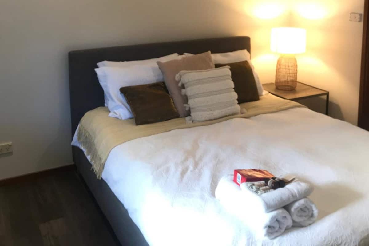 A neatly made bed with white linens, a headboard, and a bedside lamp.