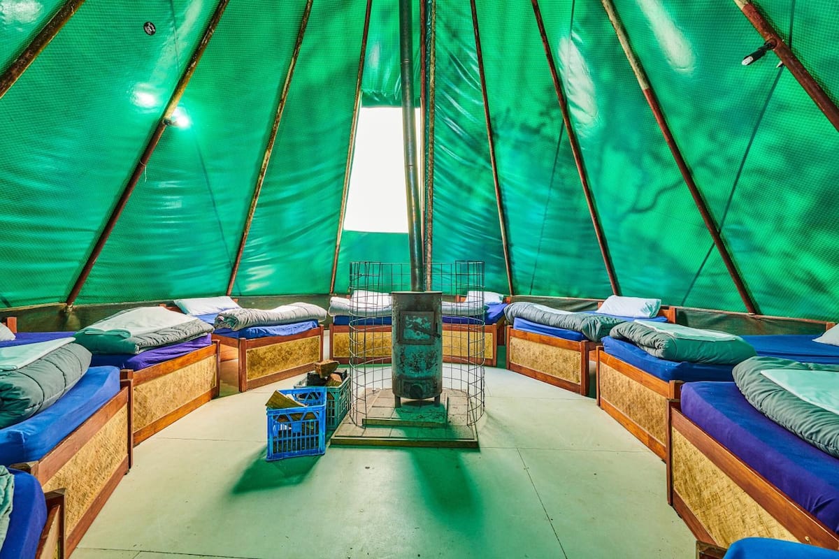 A spacious tent with multiple beds arranged in a circular pattern, a central stove, and a blue crate.