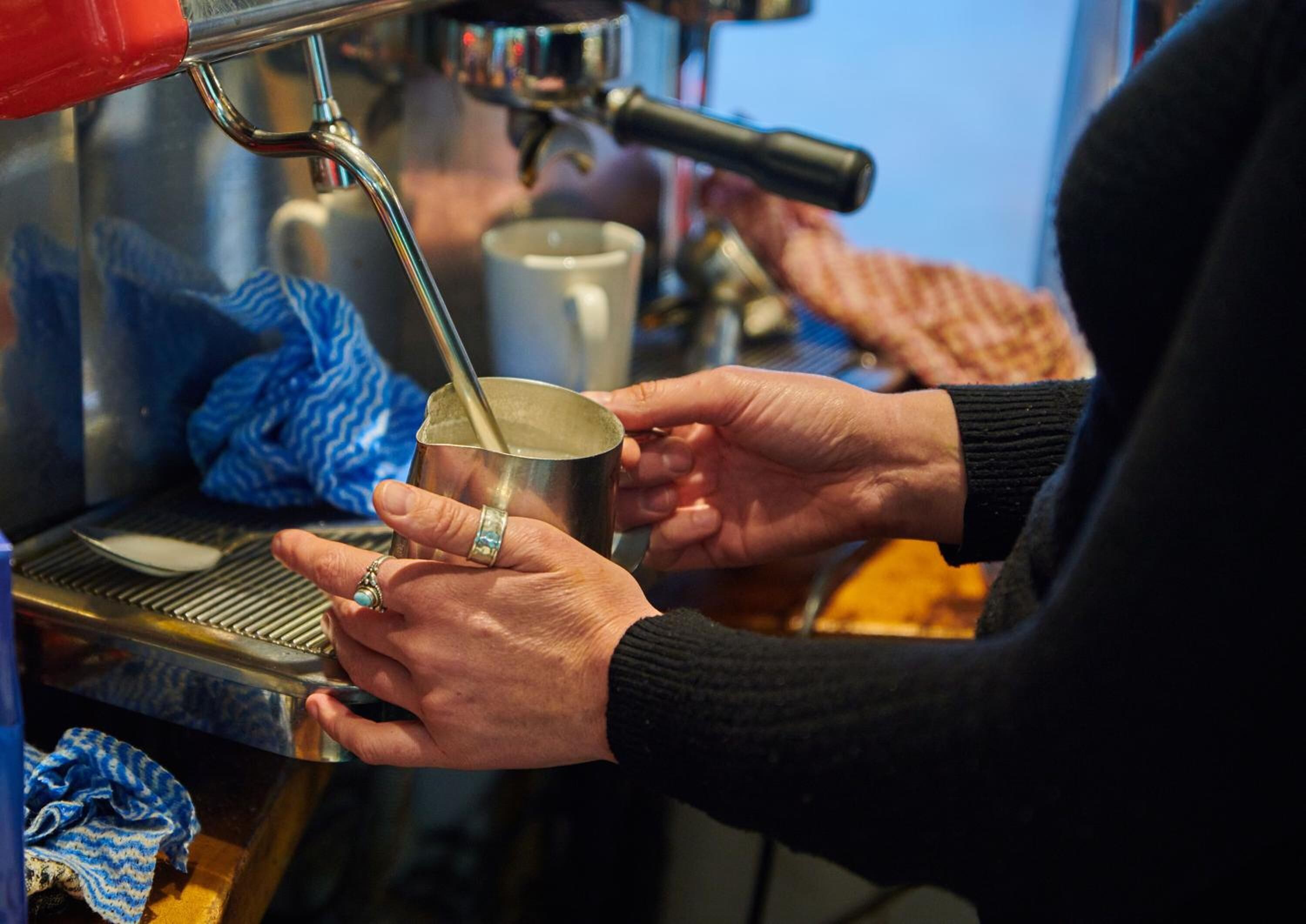 A person holding a metal cup under a coffee machine.