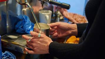 A person holding a metal cup under a coffee machine.