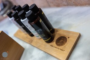 Una bandeja de madera con varias botellas de aceites esenciales etiquetadas como "Lotus" y "Abeliona Retreat" sobre una superficie de mármol.