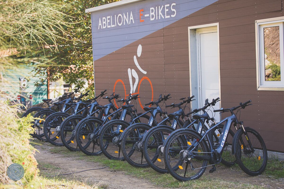 Varias bicicletas están estacionadas frente a un edificio con un letrero que dice 'ABELONA E-BIKES'.