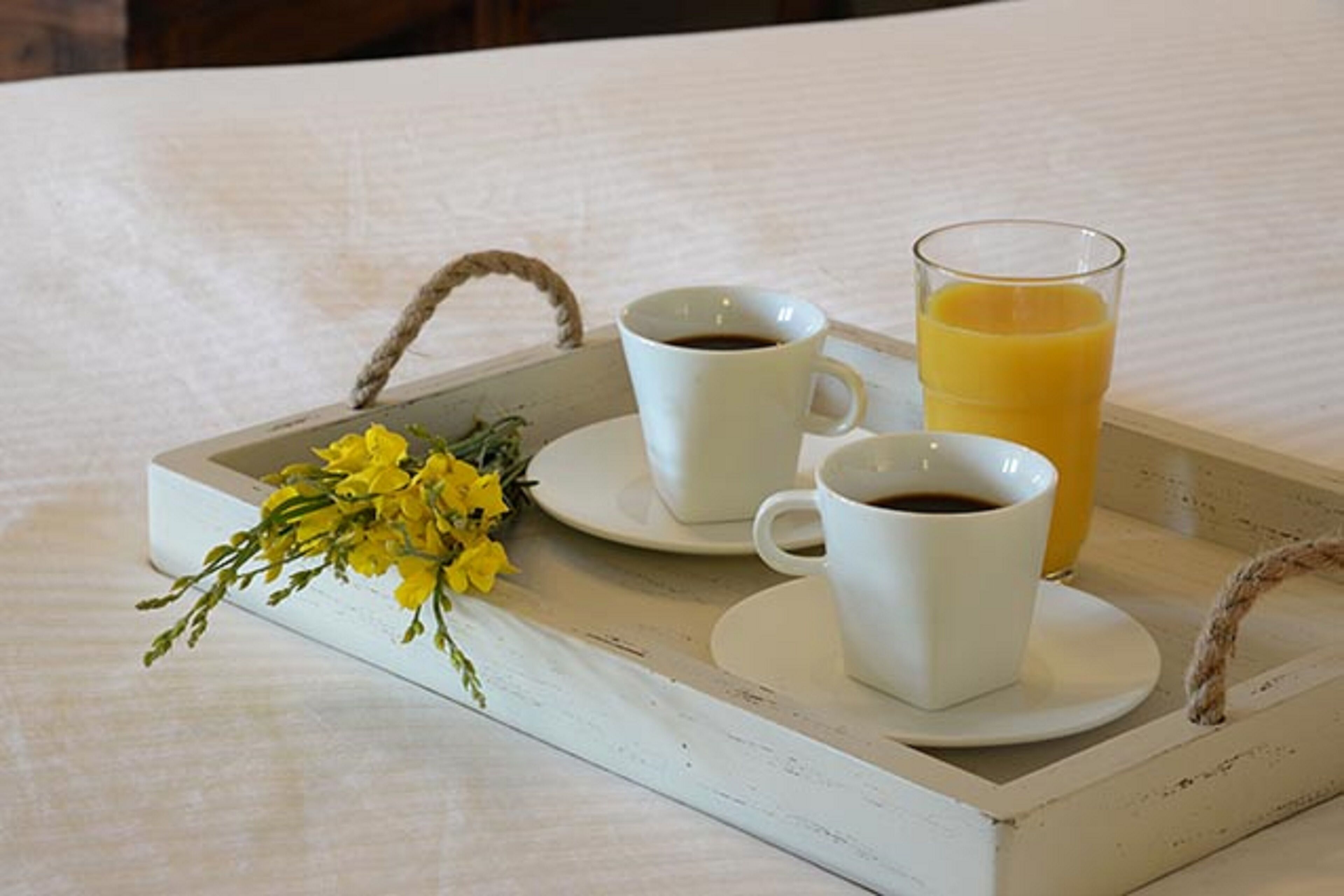 A tray with two cups of coffee and a glass of orange juice, accompanied by a small bouquet of yellow flowers.