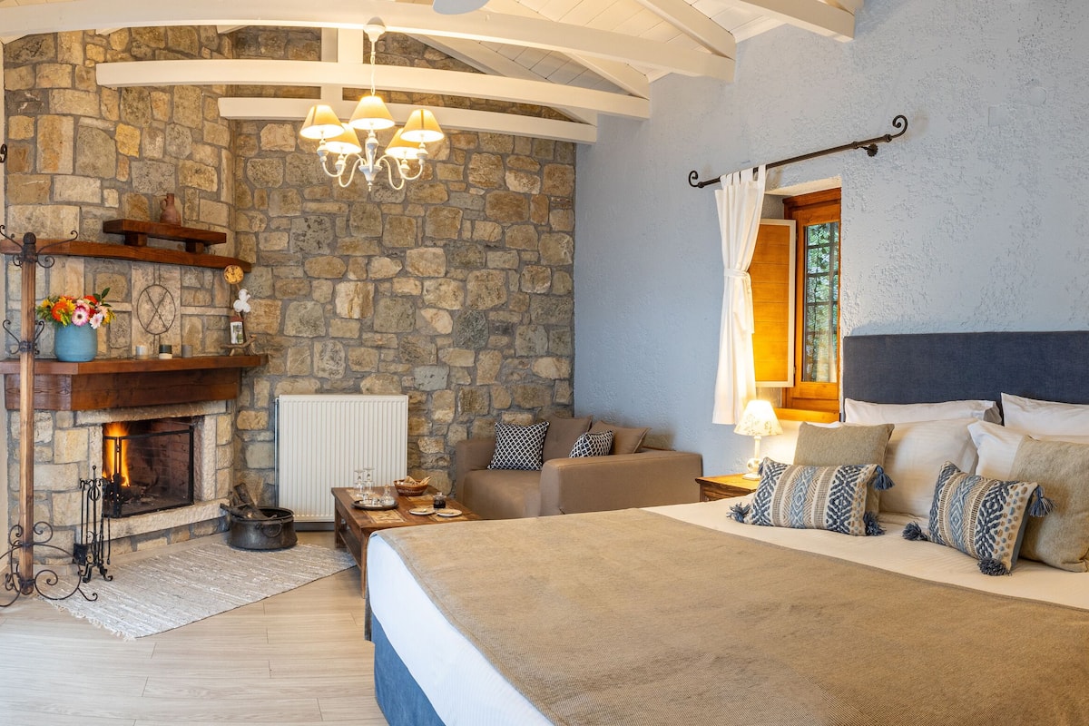 A bedroom with a stone fireplace, a bed with patterned pillows, and a chandelier.