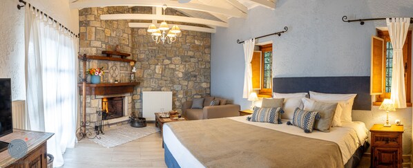 Un dormitorio con chimenea de piedra, cama con almohadones estampados y una araña.