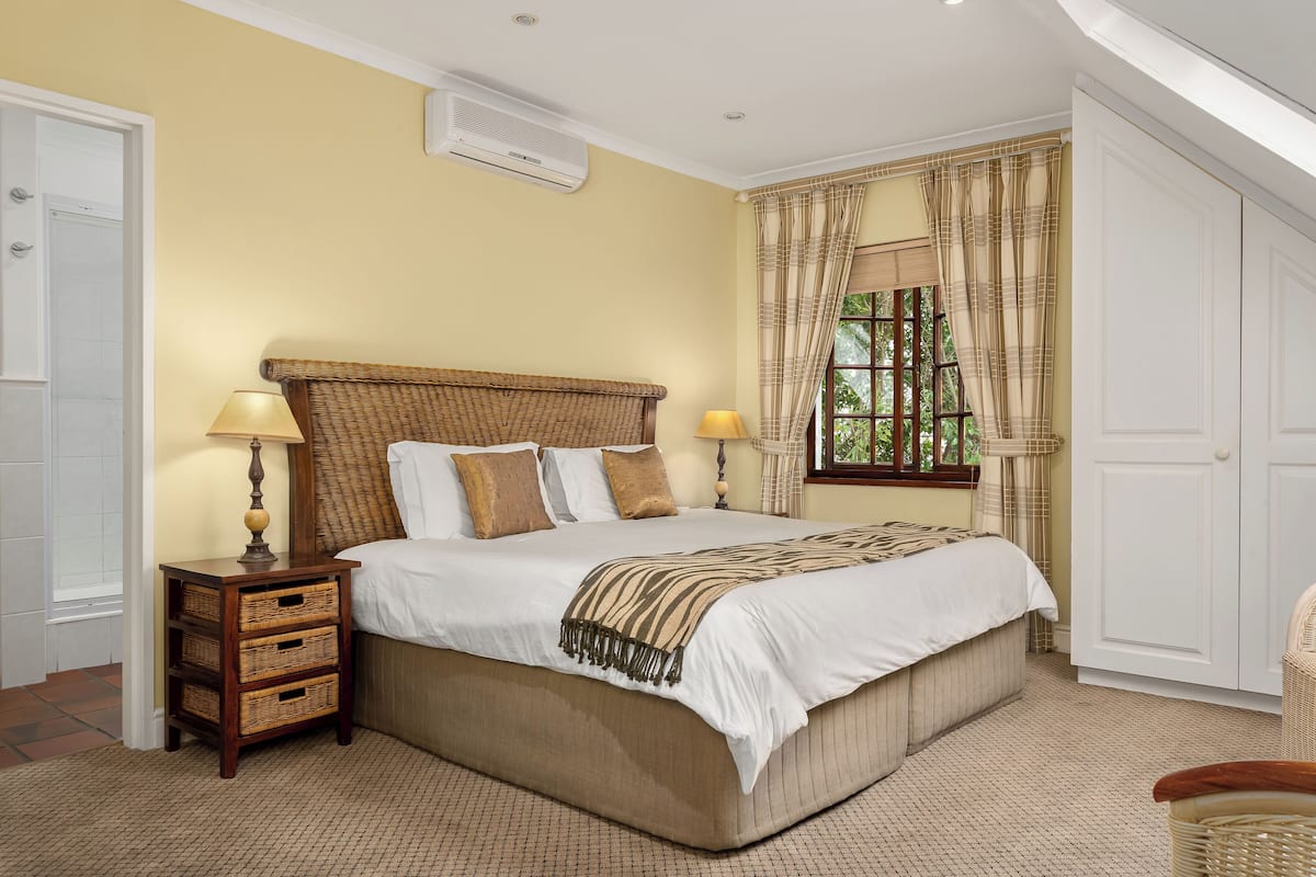 A bedroom with a bed, two bedside tables, a window with curtains, and a white door.