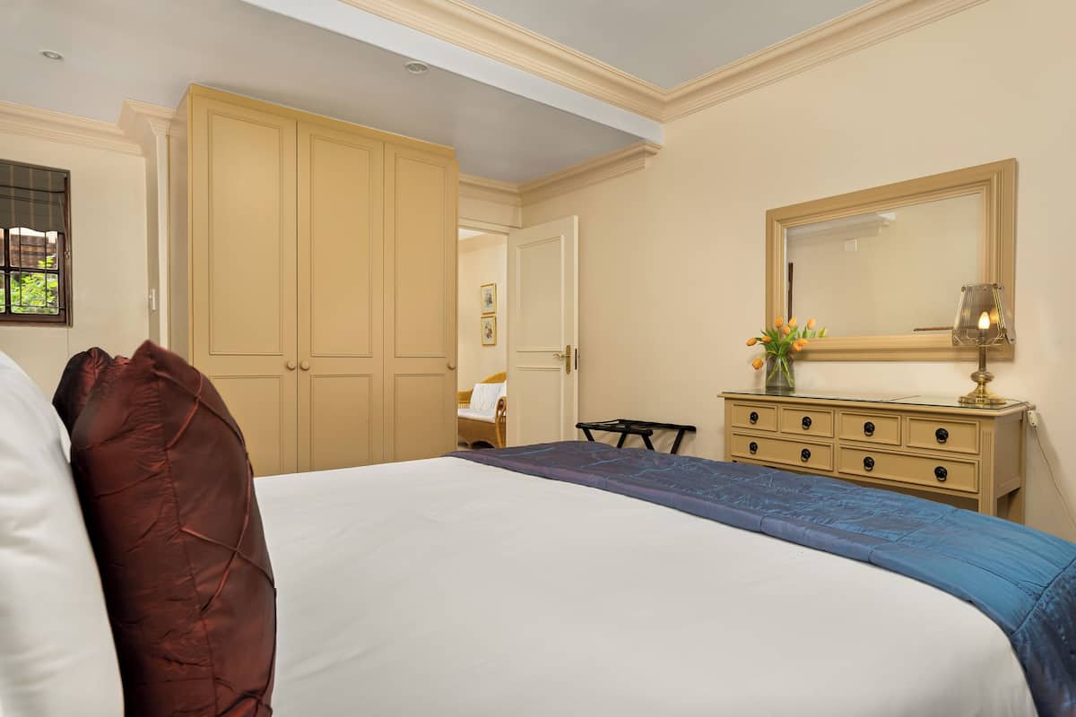 A bedroom with a large bed, a dresser, a mirror, and a window with blinds.