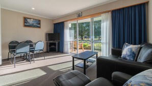 A modern living room with a sofa, a coffee table, and a dining area with chairs and a TV. - Parklands Motel (Te Anau)