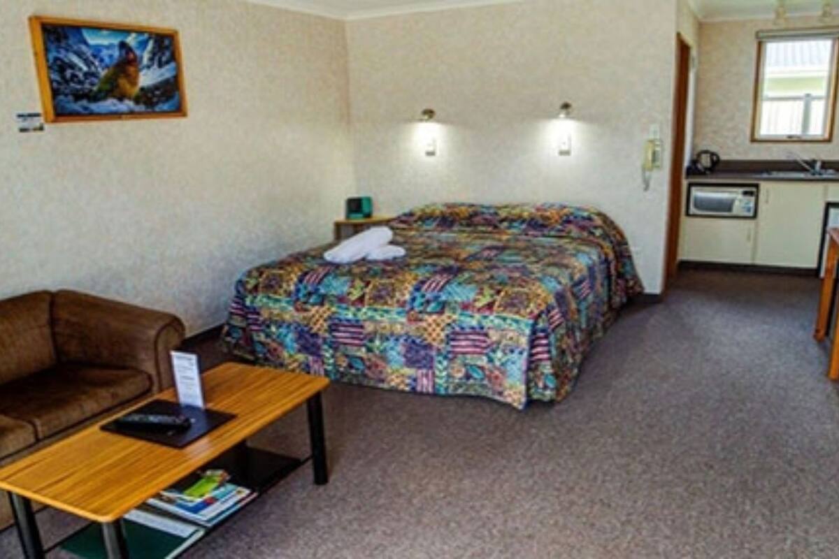 A small, furnished room with a bed, a sofa, a table, and a kitchenette.
