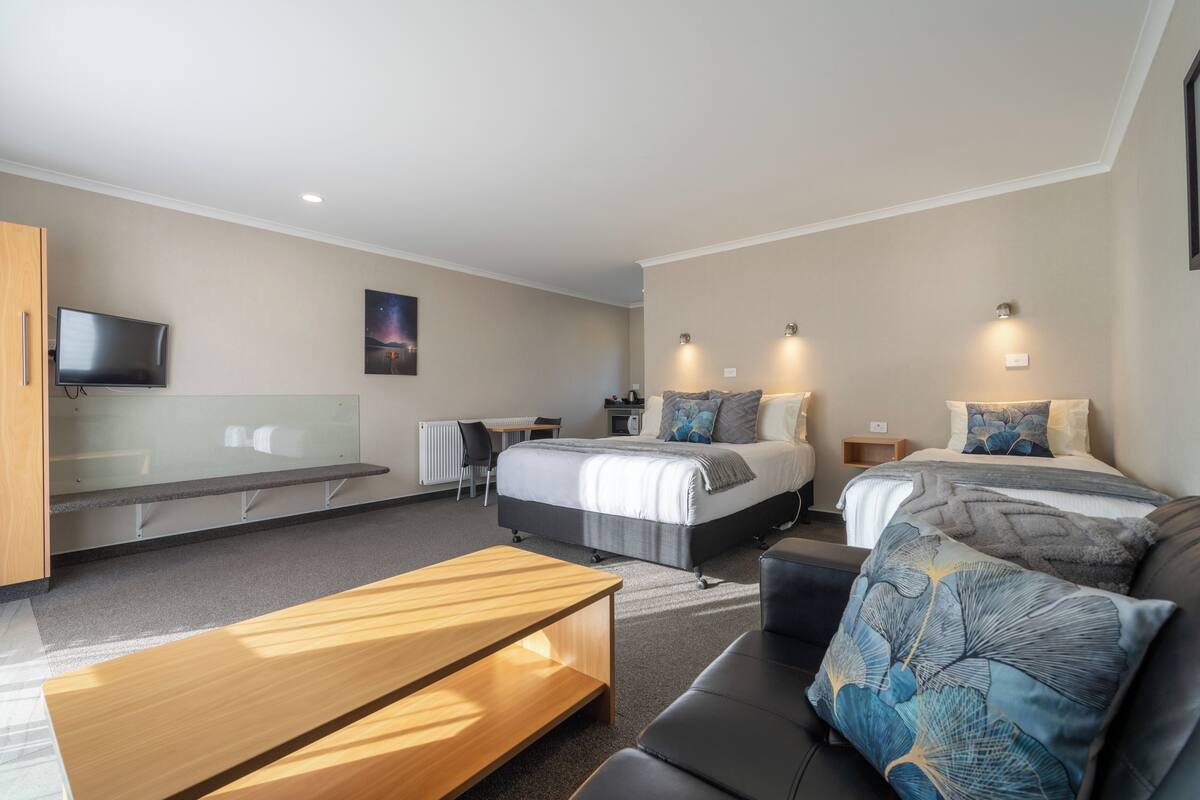 A modern hotel room with a bed, a desk, a sofa, and a TV.