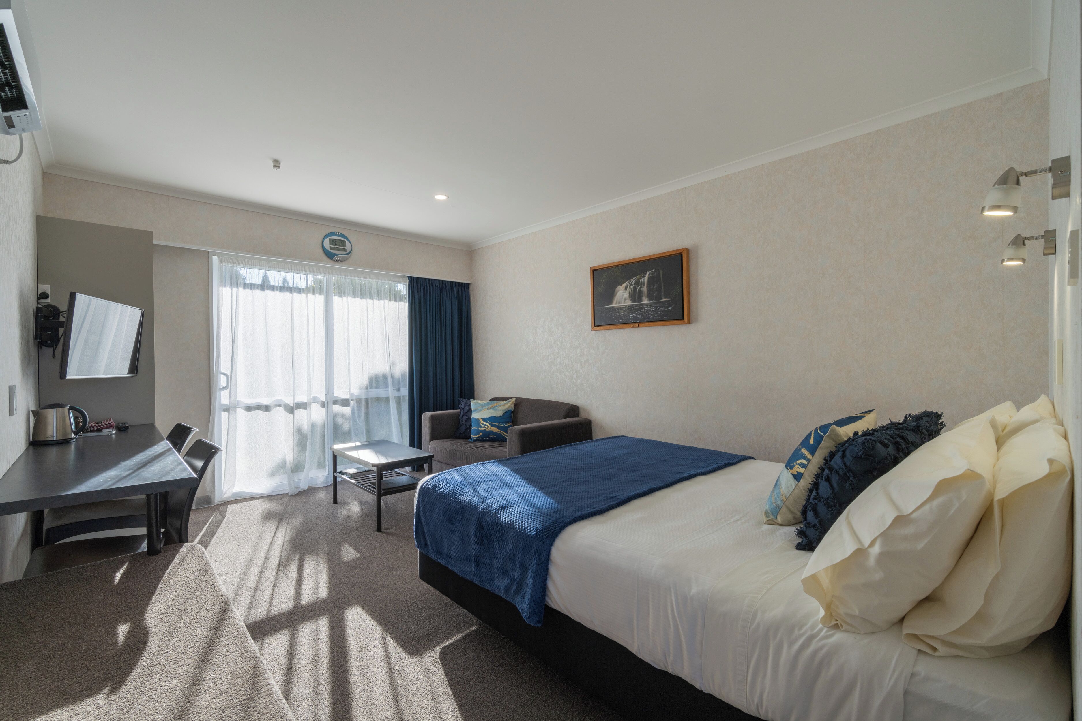A hotel room with a bed, a desk, a chair, a TV, and a window with curtains.