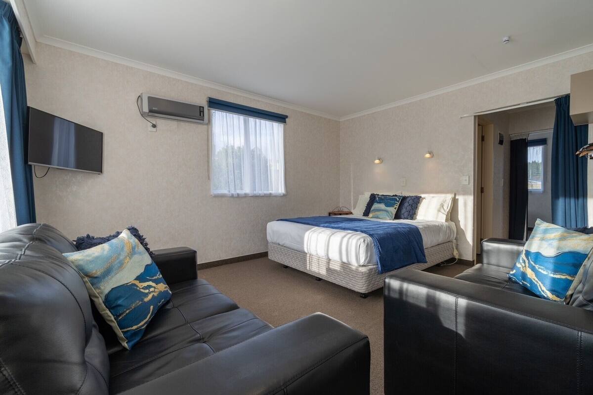 A hotel room with a bed, a sofa, a TV, and a window with curtains.