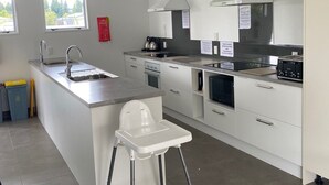A modern kitchen with white cabinets, stainless steel appliances, a built-in island with a sink, and a high chair. - Parklands Motel (Te Anau)