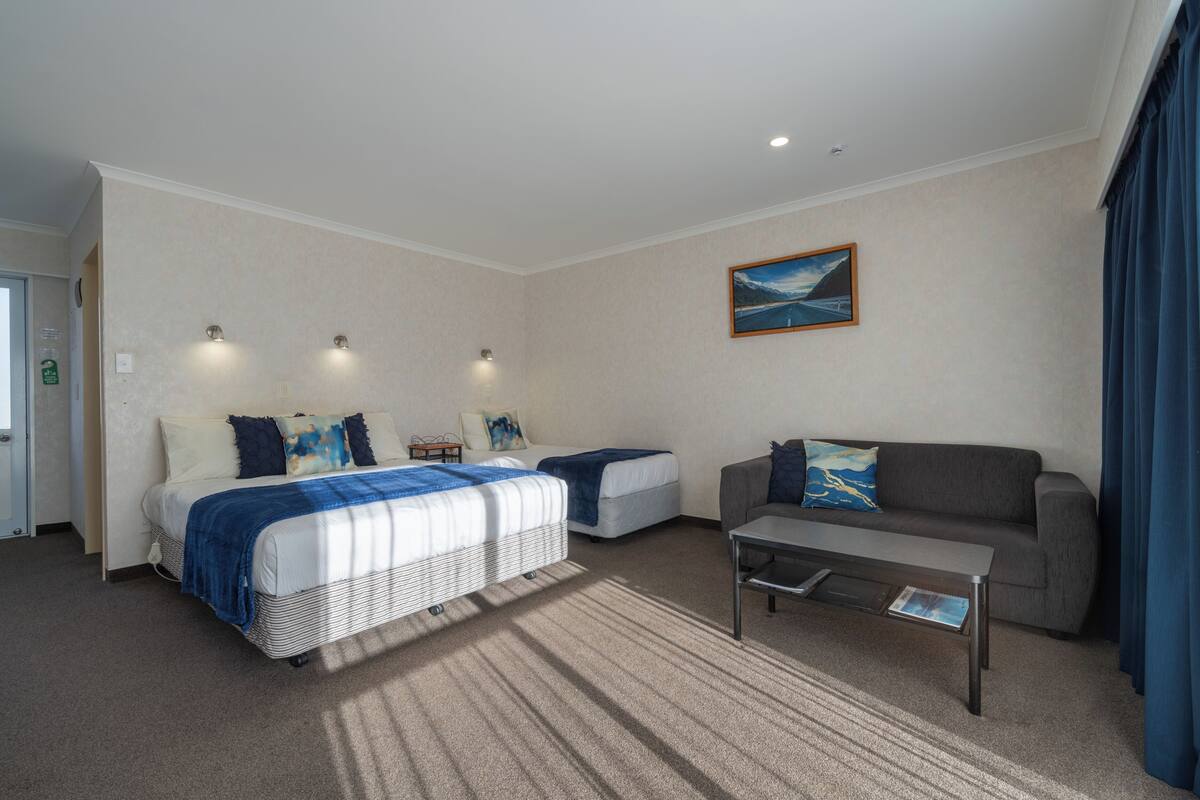 A hotel room with two beds, a sofa, a coffee table, and a painting on the wall.