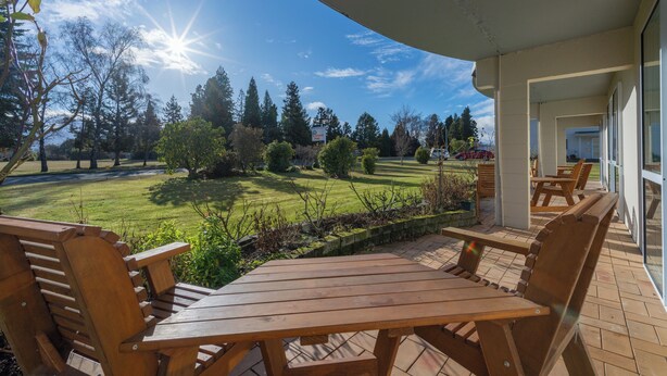 An outdoor patio with wooden furniture, a view of a well-maintained lawn, and a clear sky. - Parklands Motel (Te Anau)