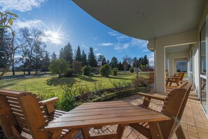An outdoor patio with wooden furniture, a view of a well-maintained lawn, and a clear sky. - Parklands Motel (Te Anau)
