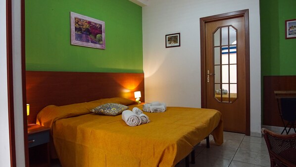 A hotel room with a bed, a nightstand, a lamp, a door with a mirror, and two framed pictures on the wall. - Baia di Naxos (Giardini Naxos)