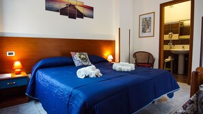 Habitación de hotel con una cama grande, una mesita de noche con lámpara, una silla y un baño visible a través de una puerta abierta.