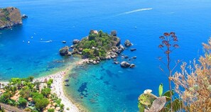A coastal area with a small island, clear blue waters, and a beach. - Baia di Naxos (Giardini Naxos)