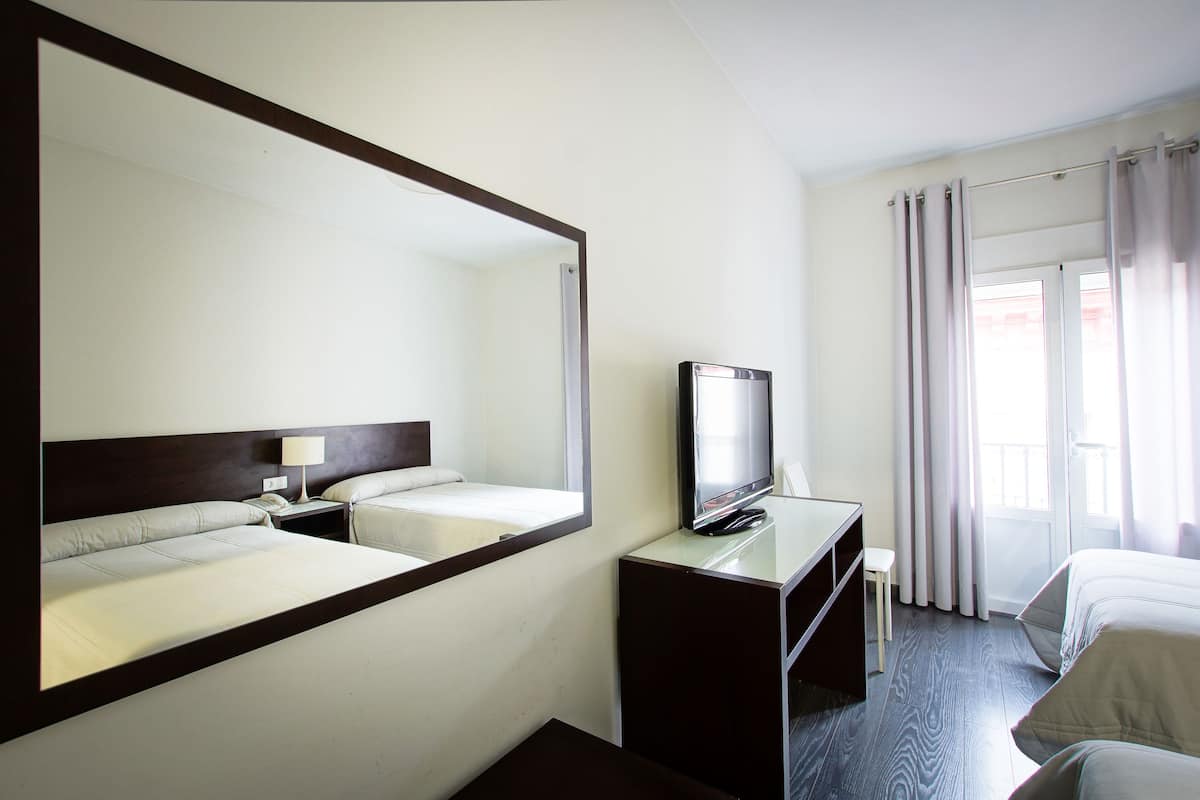 A hotel room with a large mirror, two beds, a TV, and a desk.