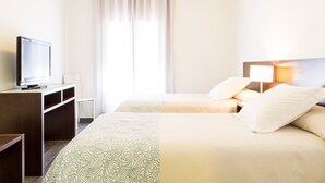 Een hotelkamer met twee bedden, een televisie op een bureau en een raam met gordijnen.