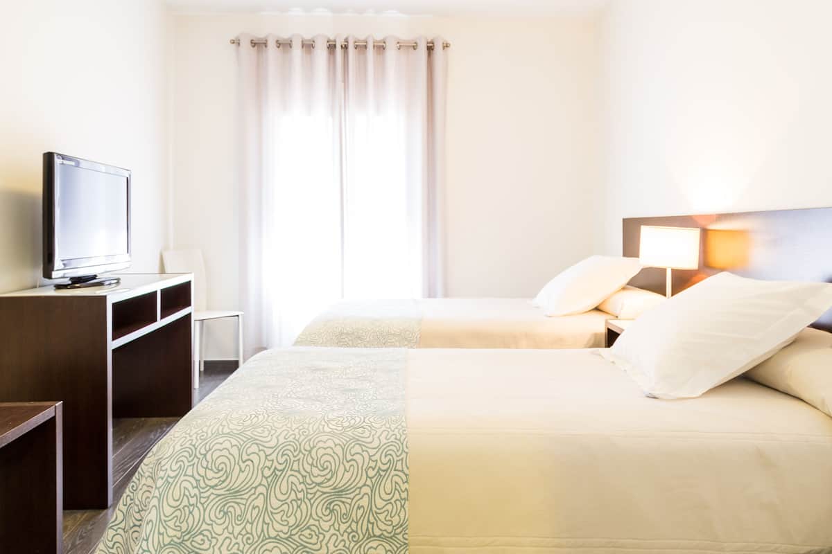 A hotel room with two beds, a TV on a desk, and a window with curtains.