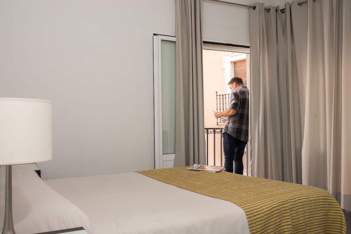 A hotel room with a bed, a bedside lamp, and a view of the outside balcony.