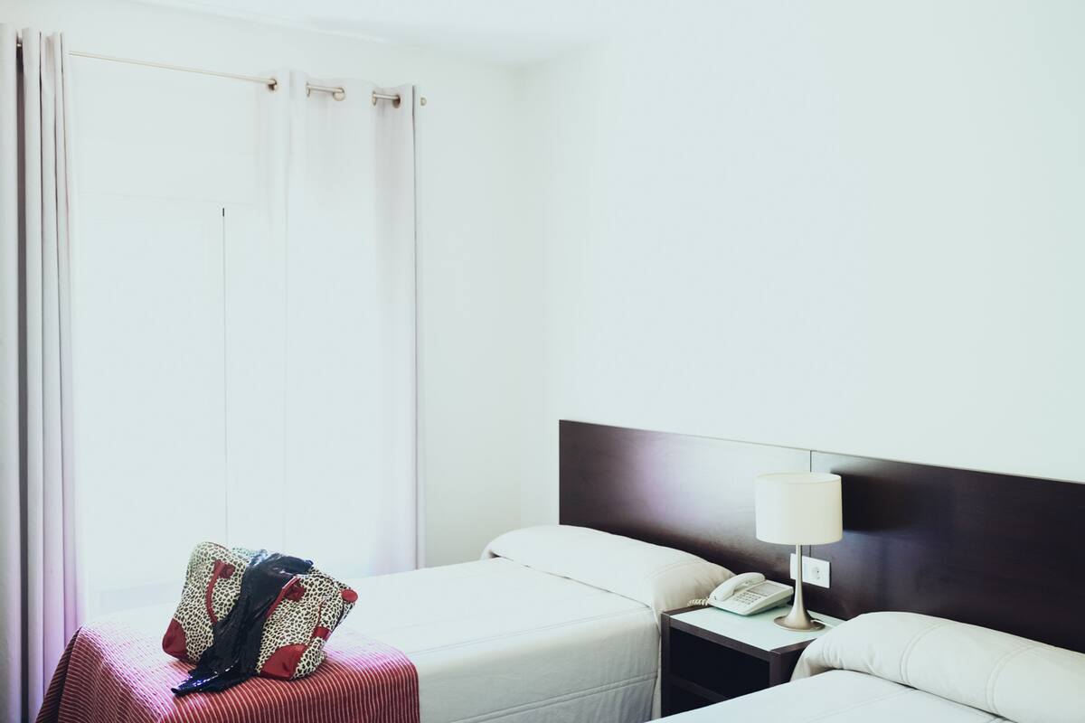 A hotel room with two beds, a bedside table with a lamp, and a telephone.