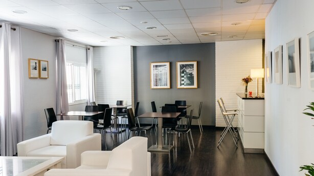Een moderne hotel lobby met een donker houten vloer, witte banken, een eetgedeelte met tafels en stoelen, en lijstwerken aan de muren.