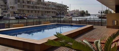 A swimming pool on a wooden deck with a view of boats and buildings in the background.