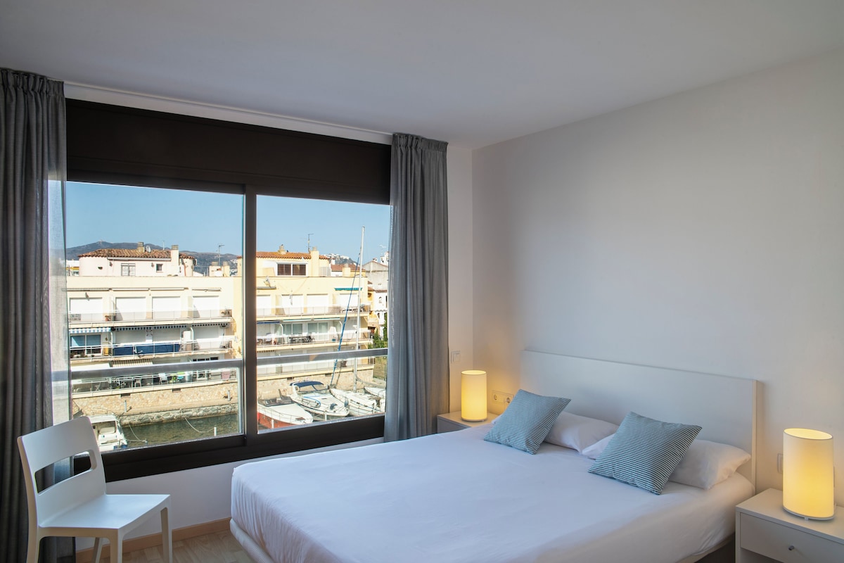 Ein Hotelzimmer mit großem Fenster, einem Bett, einem Sessel und zwei Nachttischlampen.