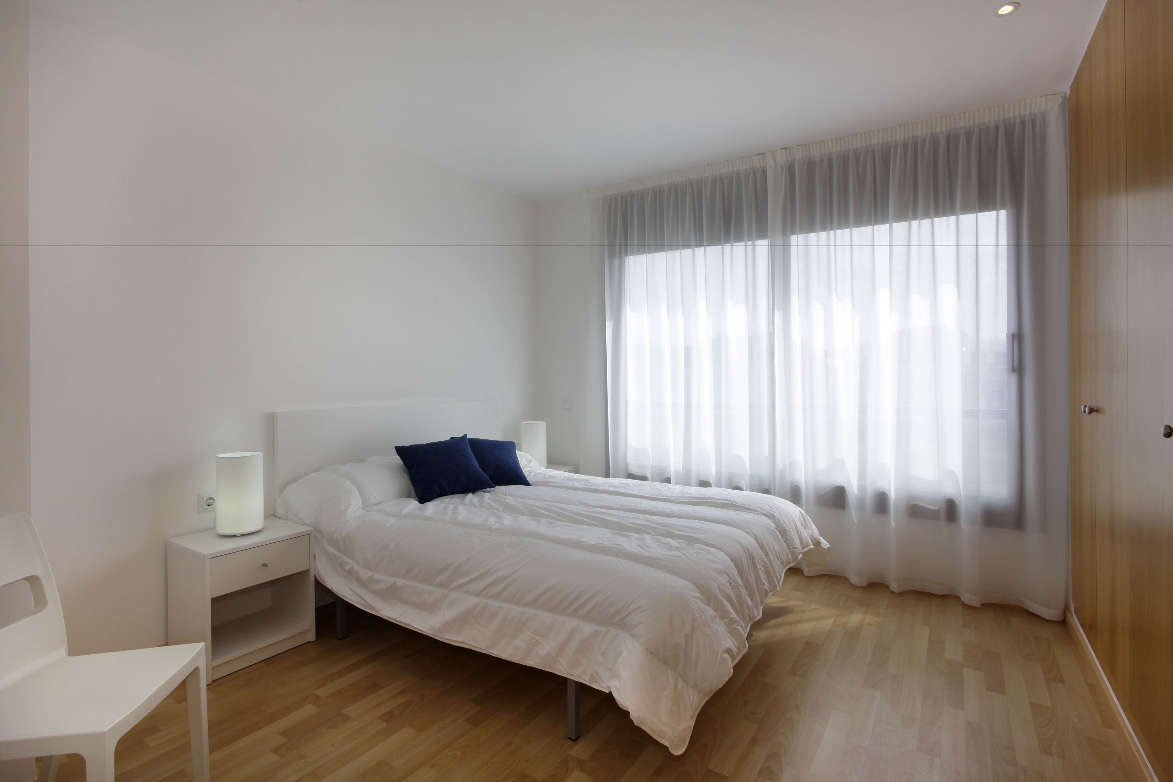 A modern bedroom with a large bed, a bedside table with a lamp, and a chair.