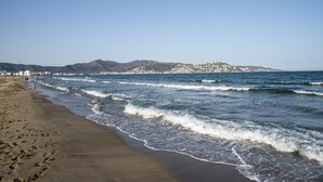 Ein Strand mit Wellen, ein ferner Berg und einige Gebäude.