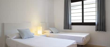 Une chambre avec deux lits simples, une table de chevet avec une lampe et une fenêtre avec des rideaux.