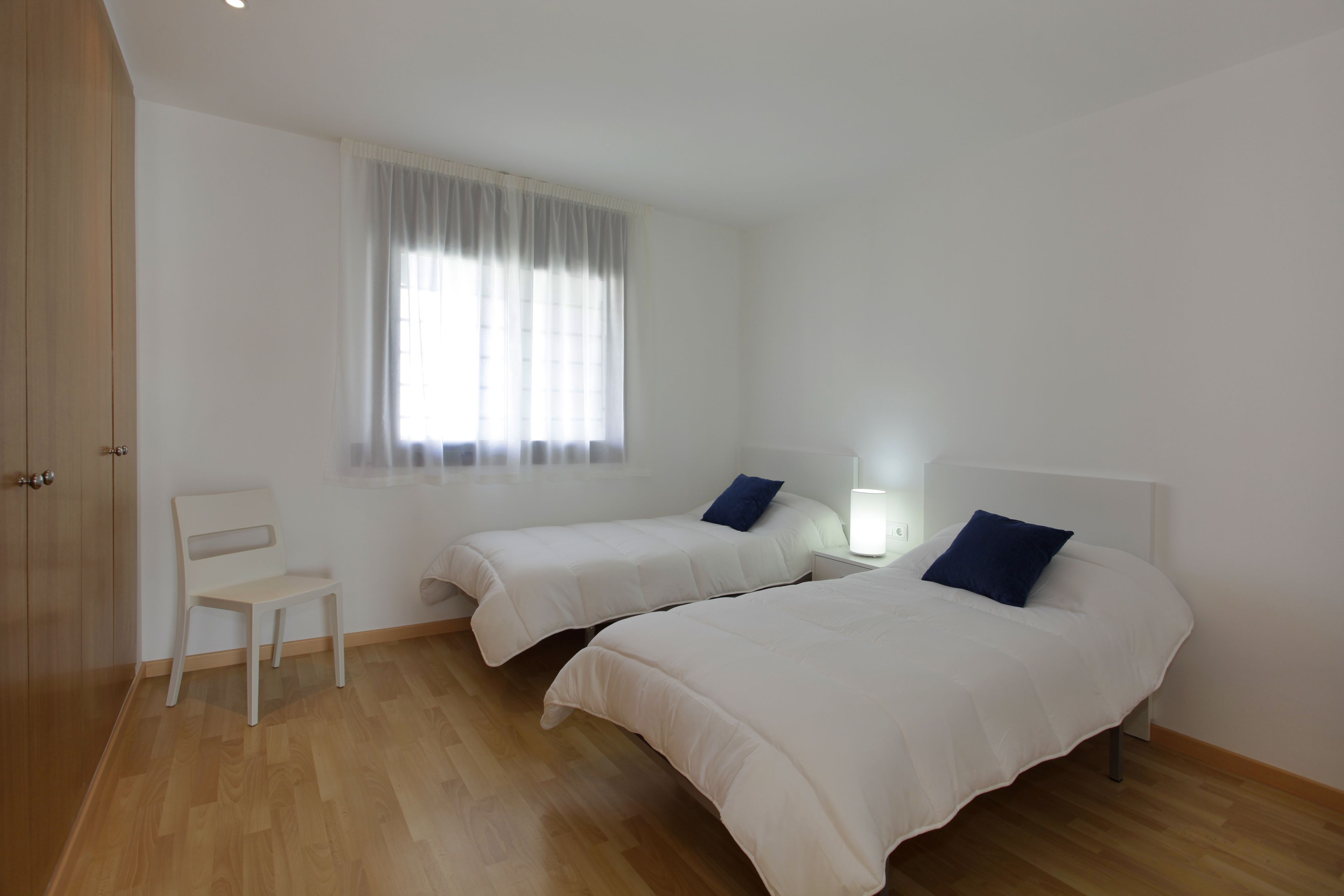 Une chambre avec deux lits, une chaise et une fenêtre avec des rideaux.