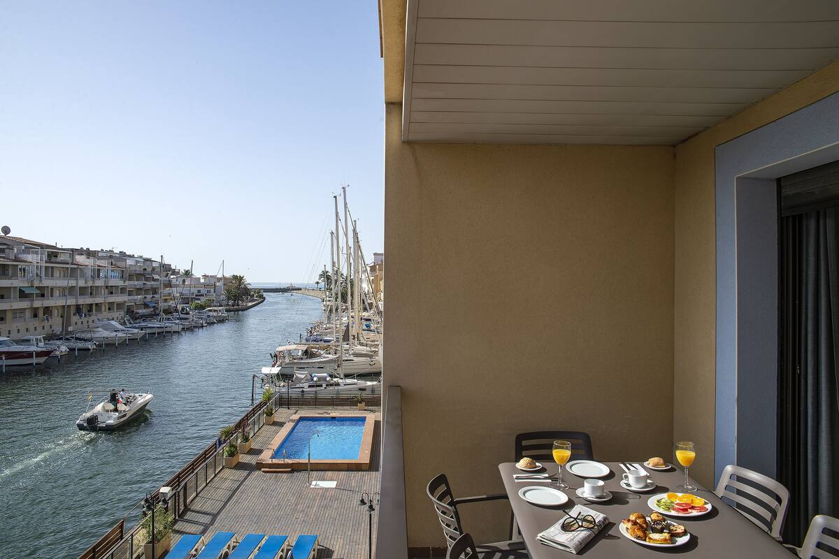 Ein Balkon mit Frühstückstisch, Blick auf einen Yachthafen mit Booten und einem Schwimmbad.