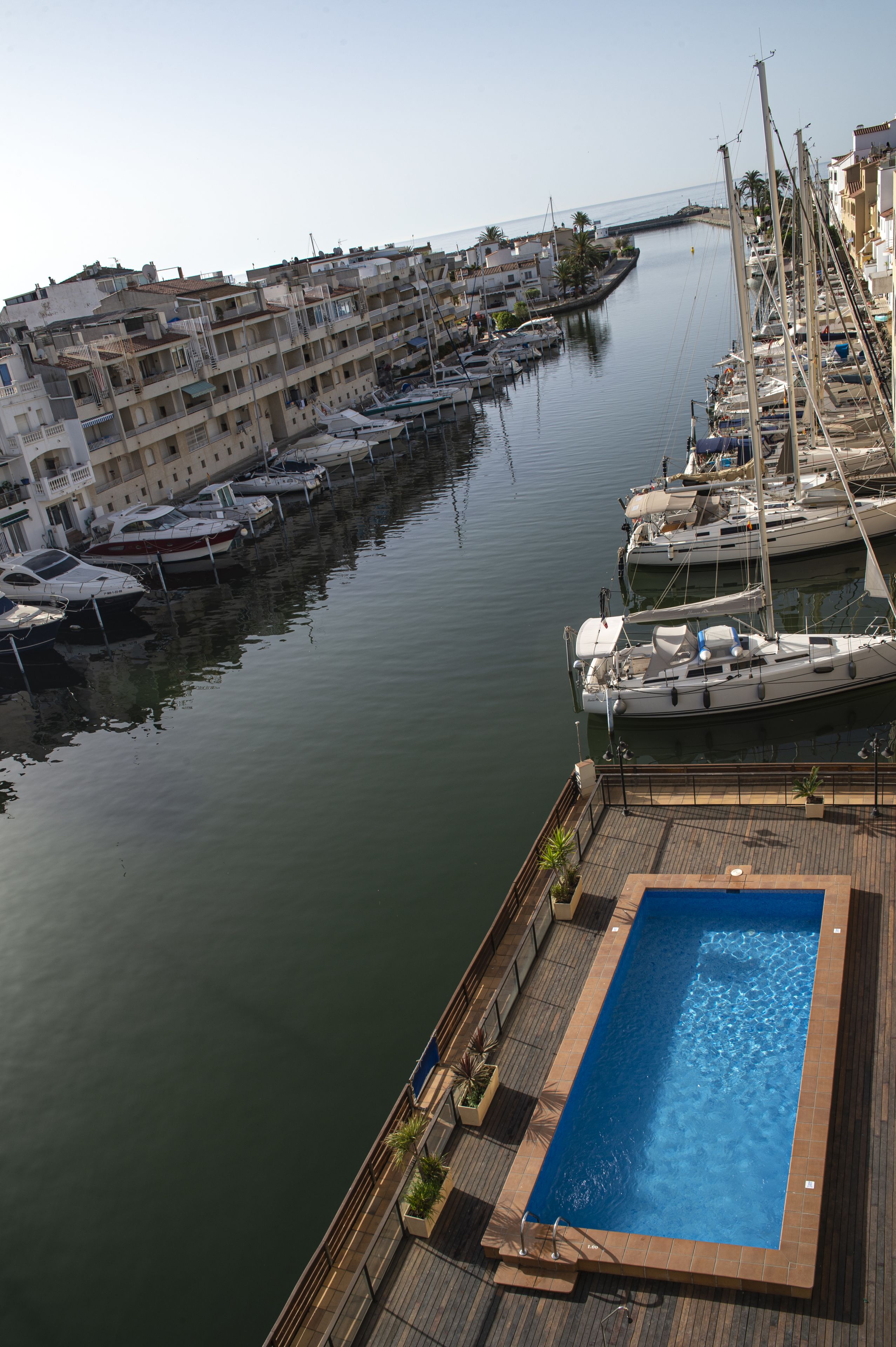Un port esportiu amb vaixells amarrats, una piscina i vista a la ciutat.