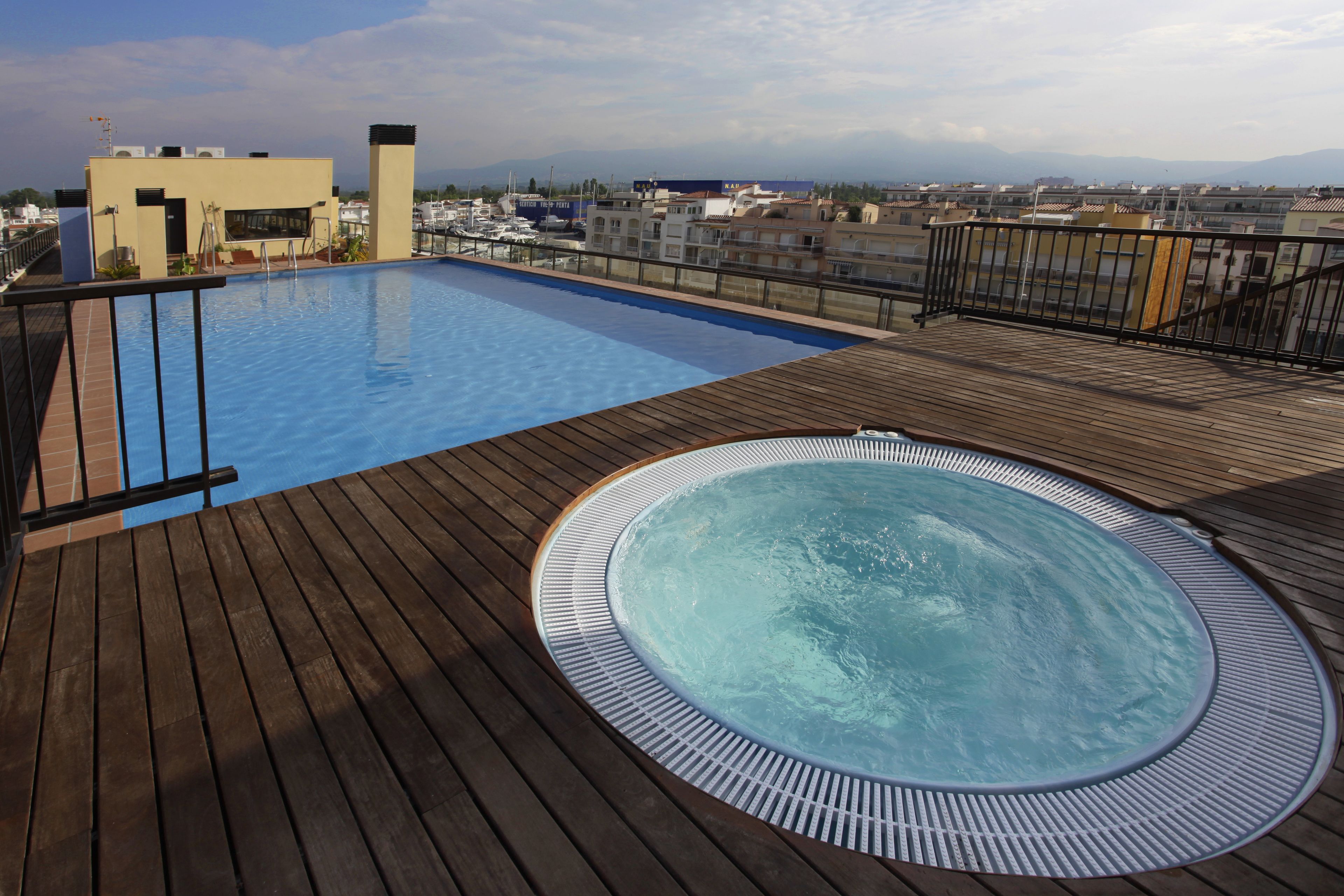 A rooftop pool with a hot tub, wooden deck, and a view of the cityscape.
