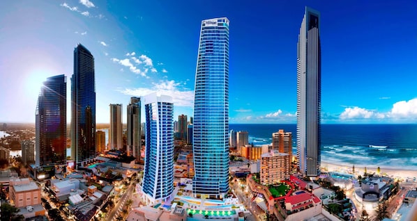Un moderno complejo hotelero con varios edificios altos, vistas a la playa y un entorno urbano bien iluminado.