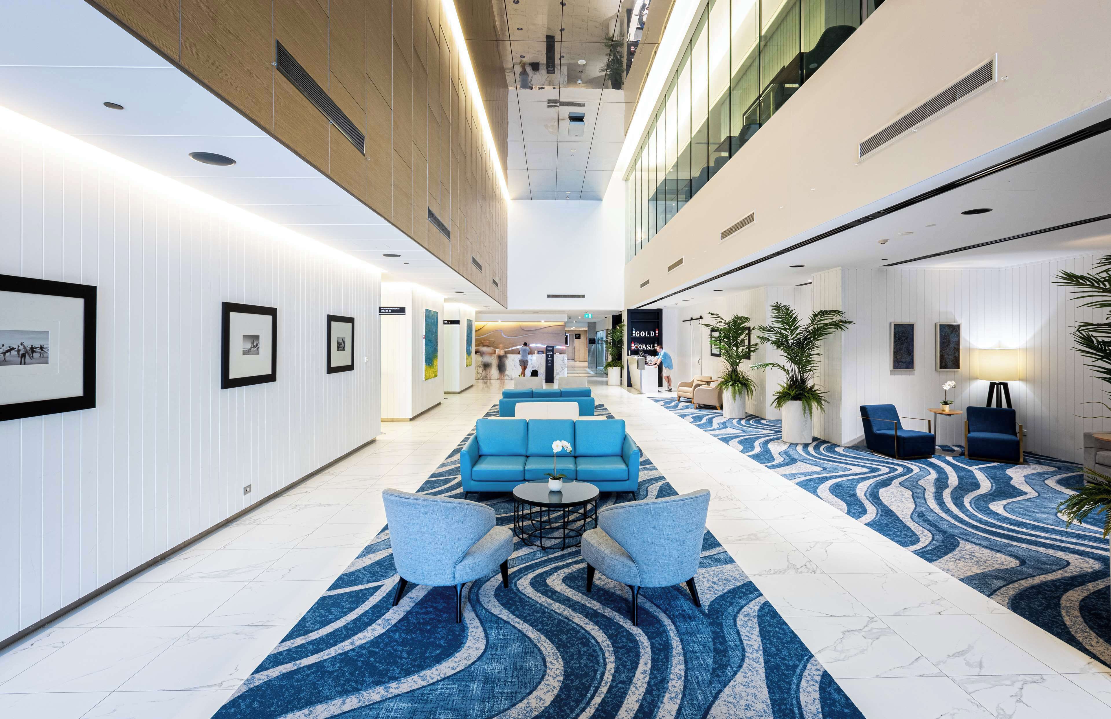 Un hall d’hôtel moderne, avec un canapé bleu, une moquette à motifs et des œuvres d’art encadrées accrochées aux murs.
