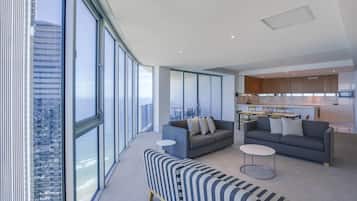 A modern living room with large windows, a sofa, a striped ottoman, and a kitchen area.