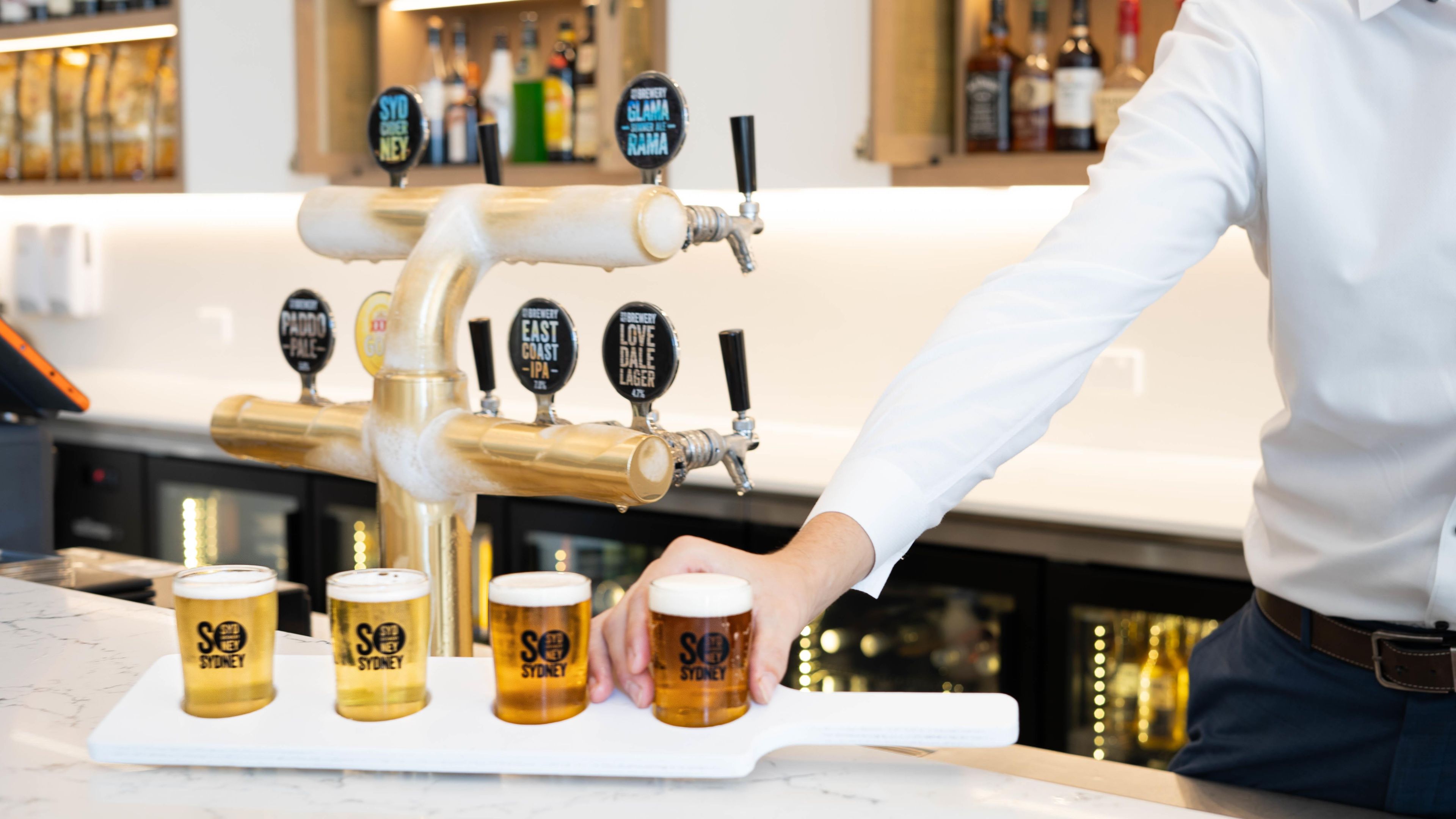 A bar setting with multiple taps and glasses labeled 'SYDNEY' on a marble countertop.