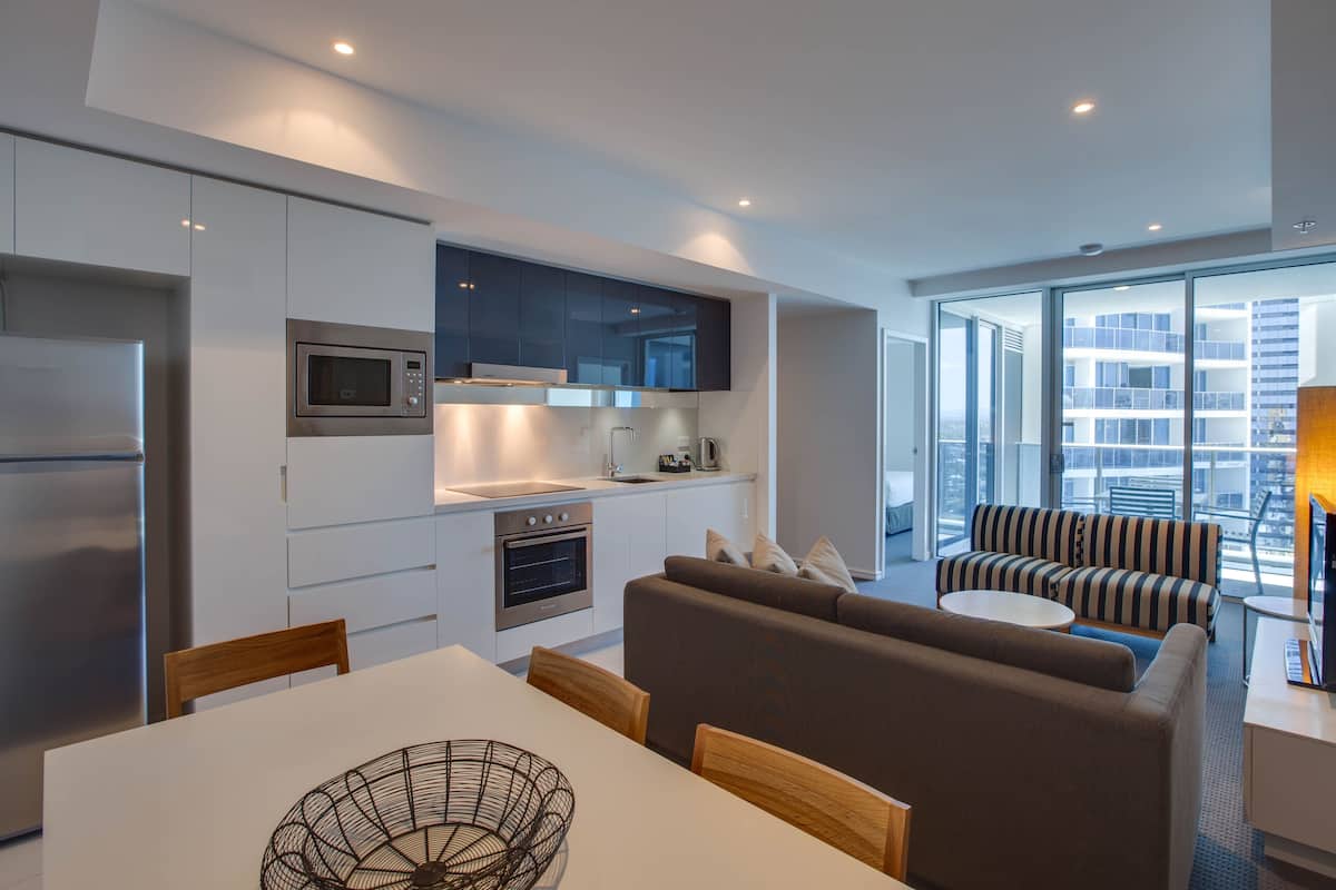 A modern kitchen with built-in appliances, a dining area with a white table and chairs, and a living area with a sofa and a coffee table.