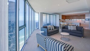 Een moderne woonkamer met grote ramen, een bank, een salontafel en een keukenhoek.