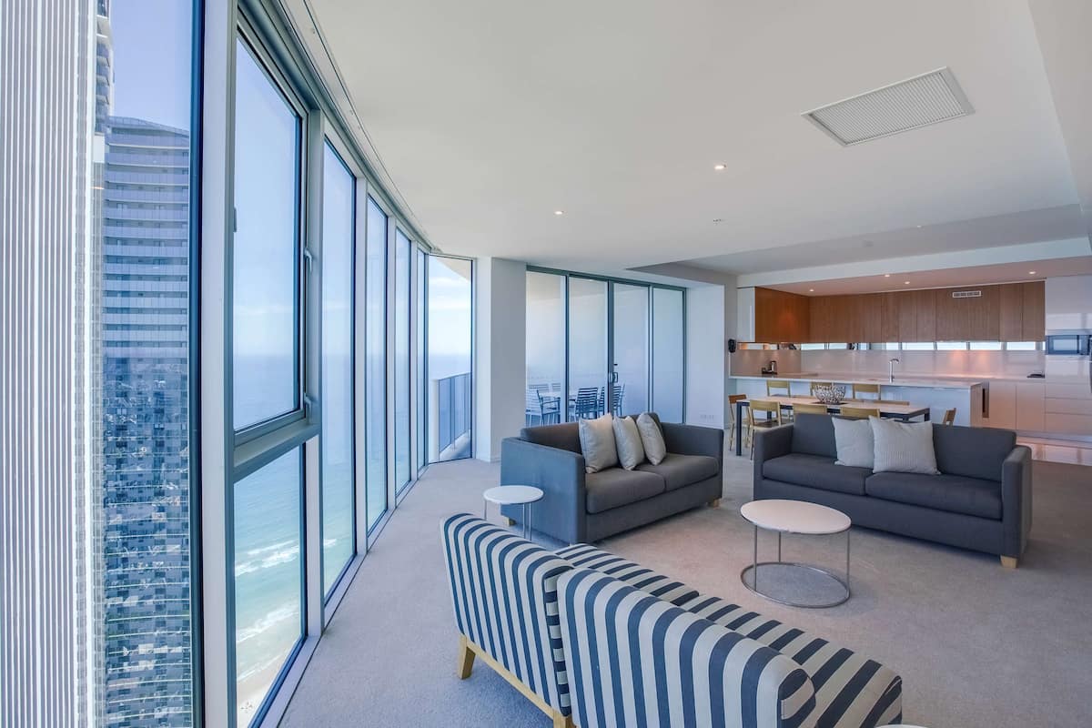 A modern living room with large windows, a sofa, a coffee table, and a kitchen area.