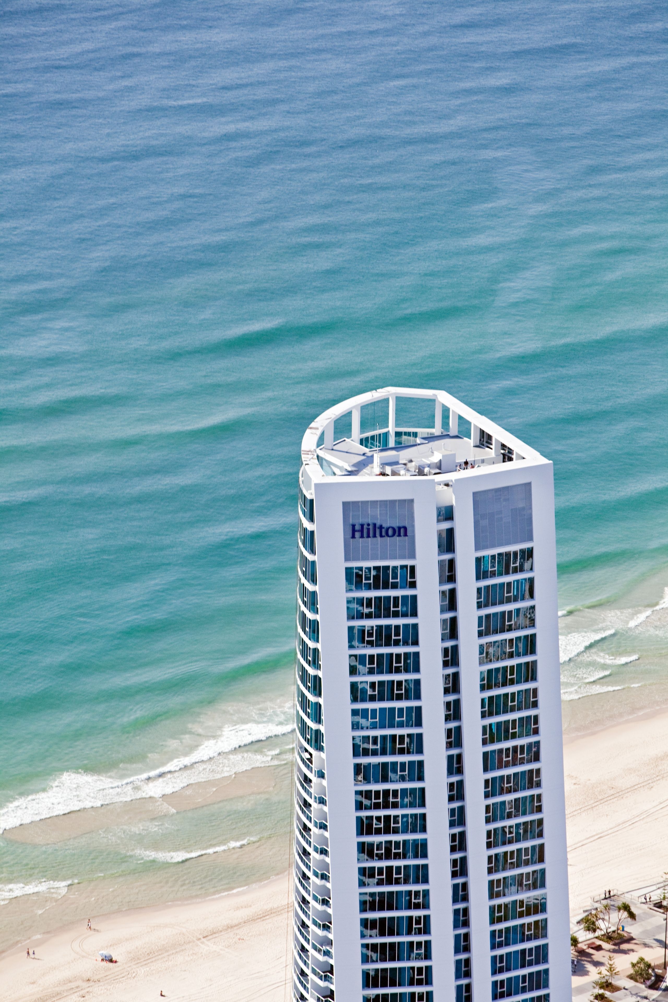 Um hotel alto e moderno com fachada de vidro e o logotipo Hilton, com vista para uma praia e o oceano.