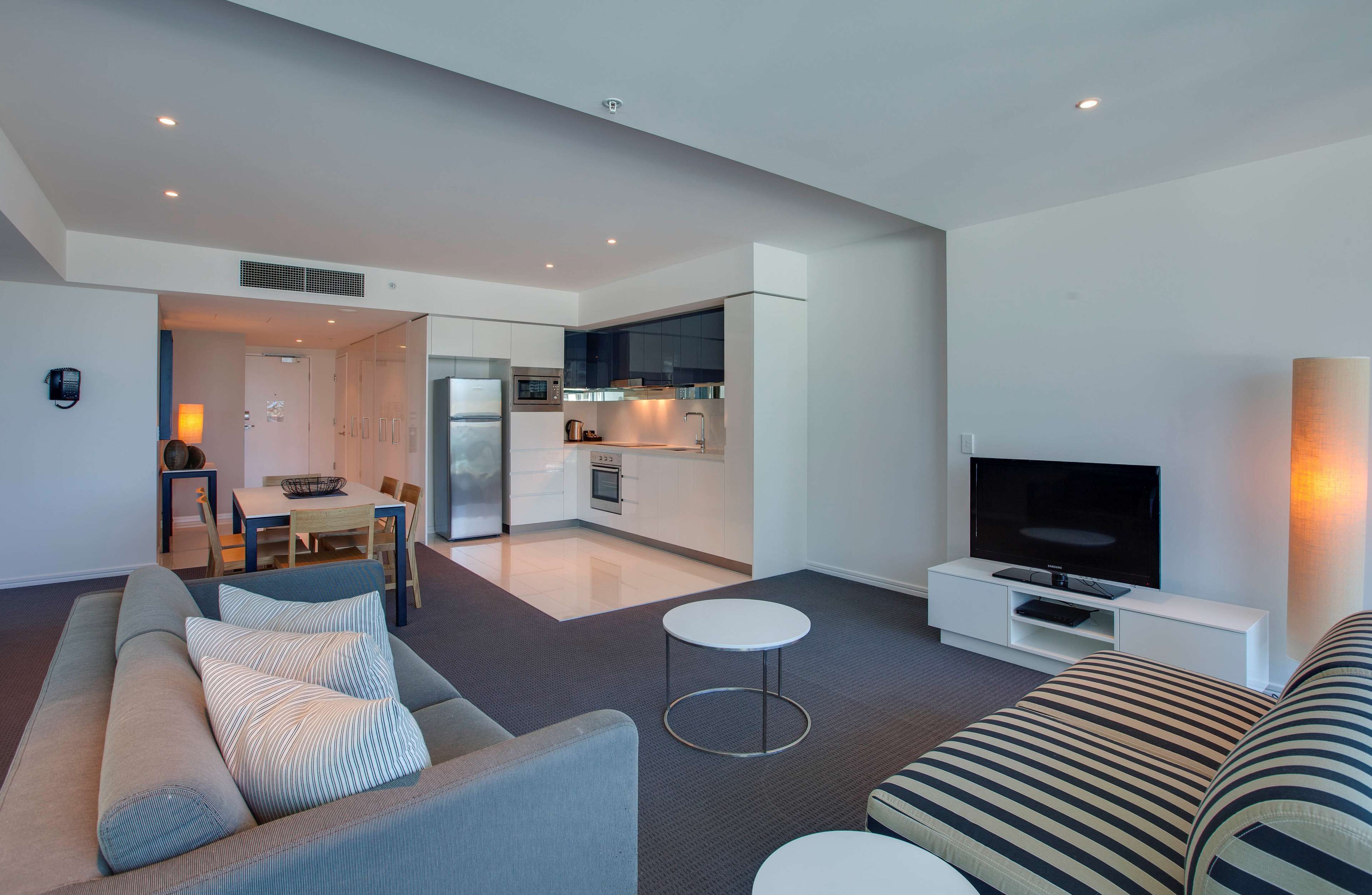 Ein modernes Wohnzimmer mit einer Couch, einem Fernseher und einem Essbereich mit Tisch und Stühlen.