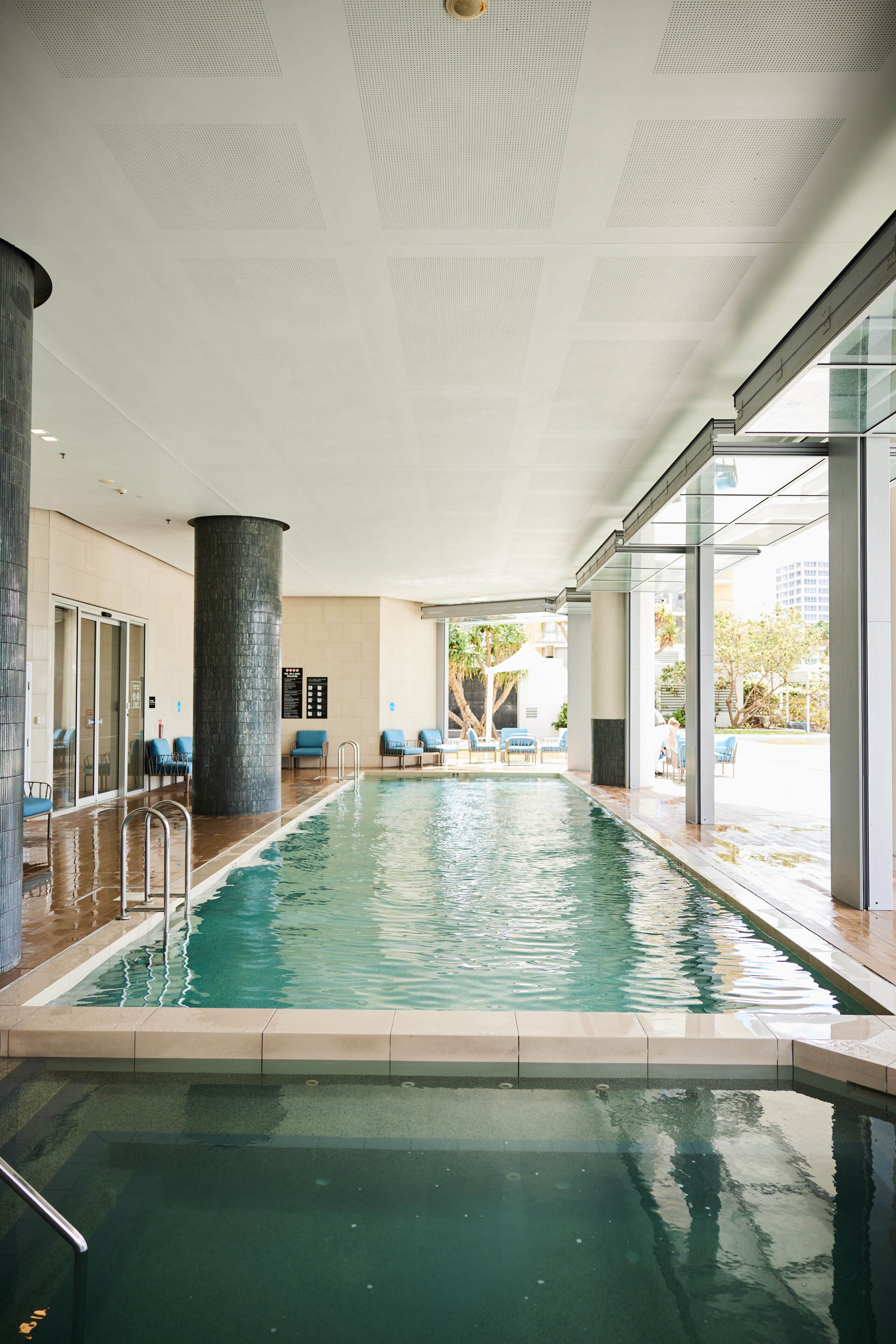 Una piscina interior con agua cristalina, rodeada de paredes de vidrio y un suelo de baldosas.