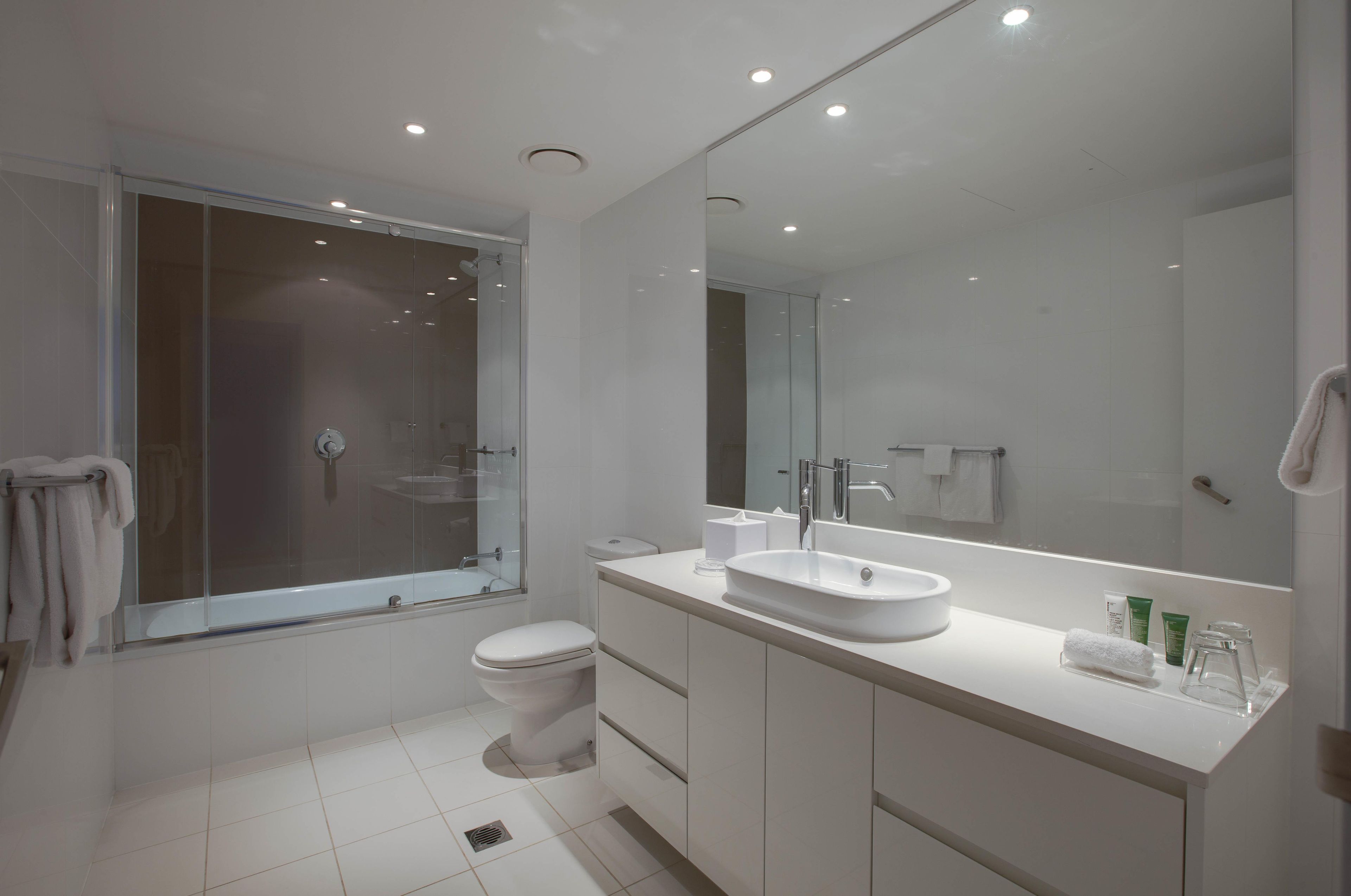 A modern bathroom with a large mirror, a sink, and a toilet.